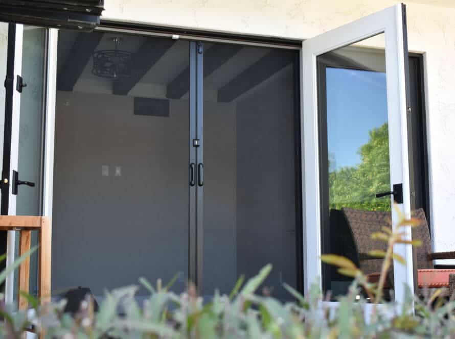 Retractable screen doors installed on a patio door, allowing fresh air while keeping insects out. The black mesh blends seamlessly with the open outdoor space.